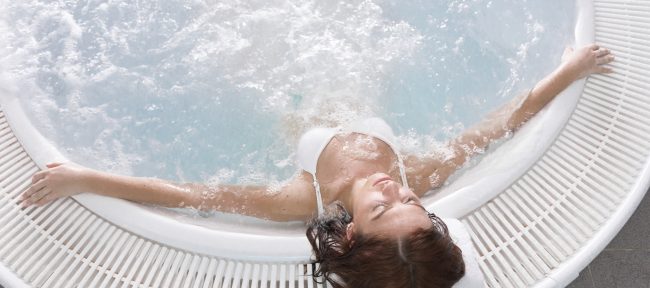 Young woman leaning back in hot tub with eyes closed