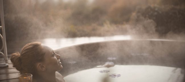 Woman relaxing in hot tub in autumn with steam rising off the surface of the water