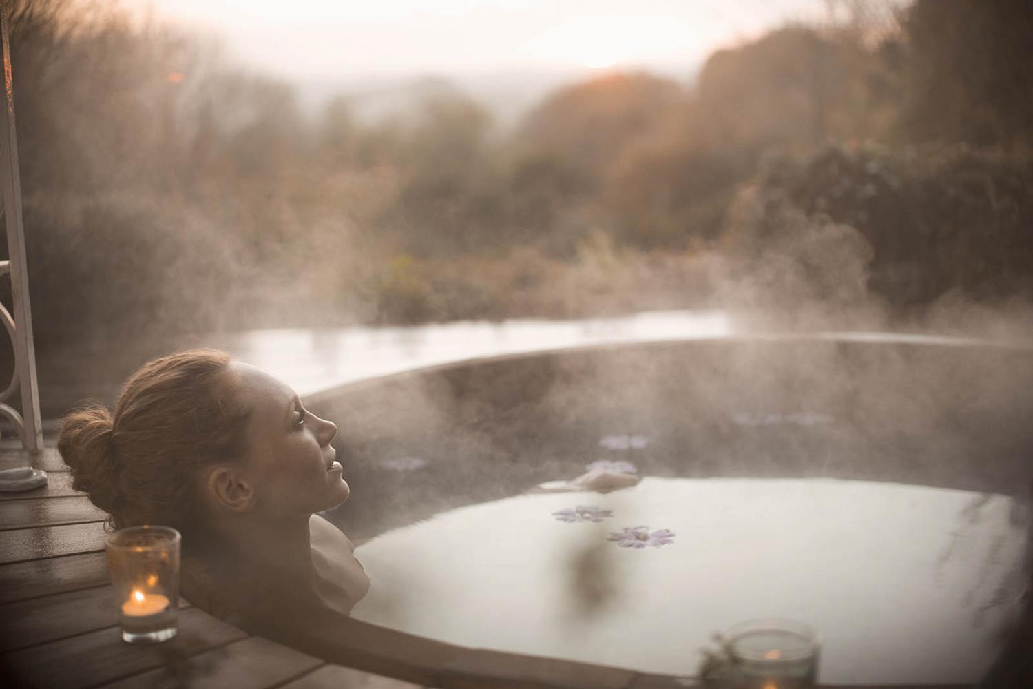 Woman relaxing in hot tub in autumn with steam rising off the surface of the water