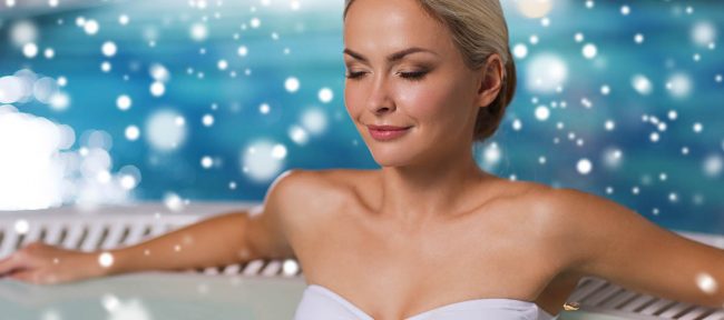 Beautiful woman wearing bikini sitting in hot tub with snow falling