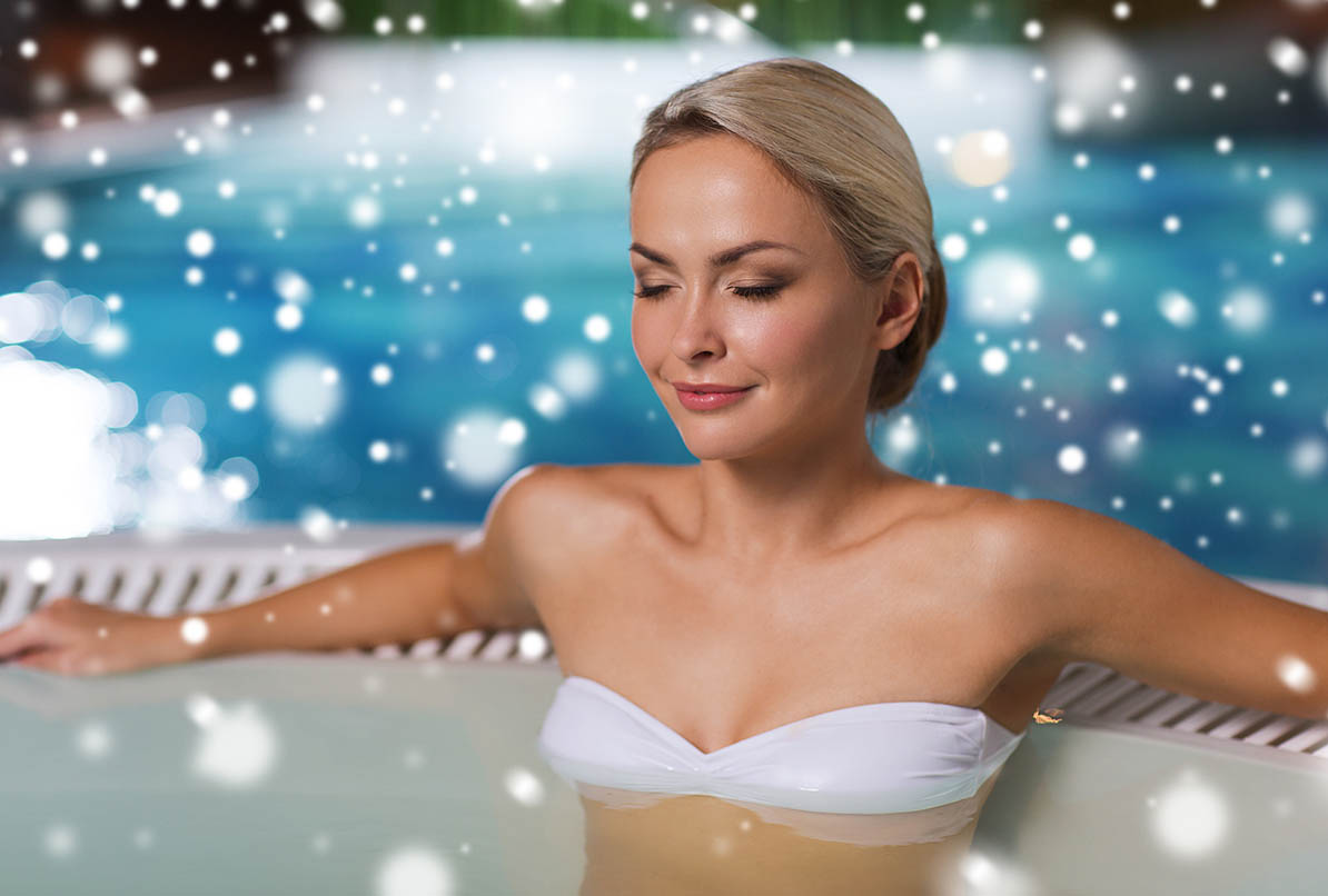 Beautiful woman wearing bikini sitting in hot tub with snow falling