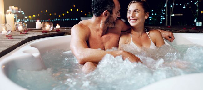 Smiling couple in hot tub with candles nearby