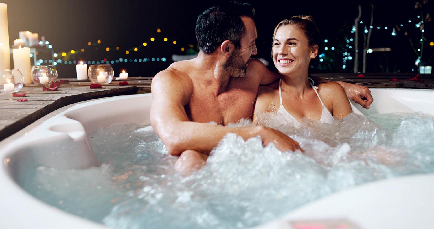 Smiling couple in hot tub with candles nearby